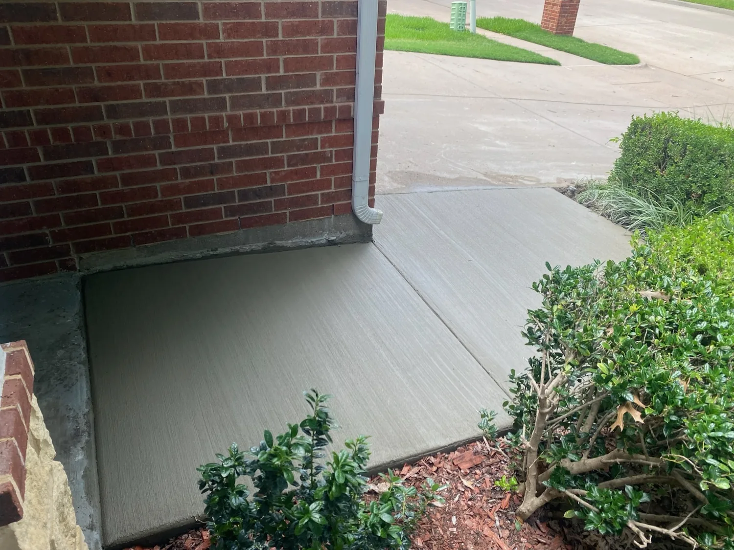 Fresh broom-finish residential concrete sidewalk wrapping a brick home corner by Billy's Concrete